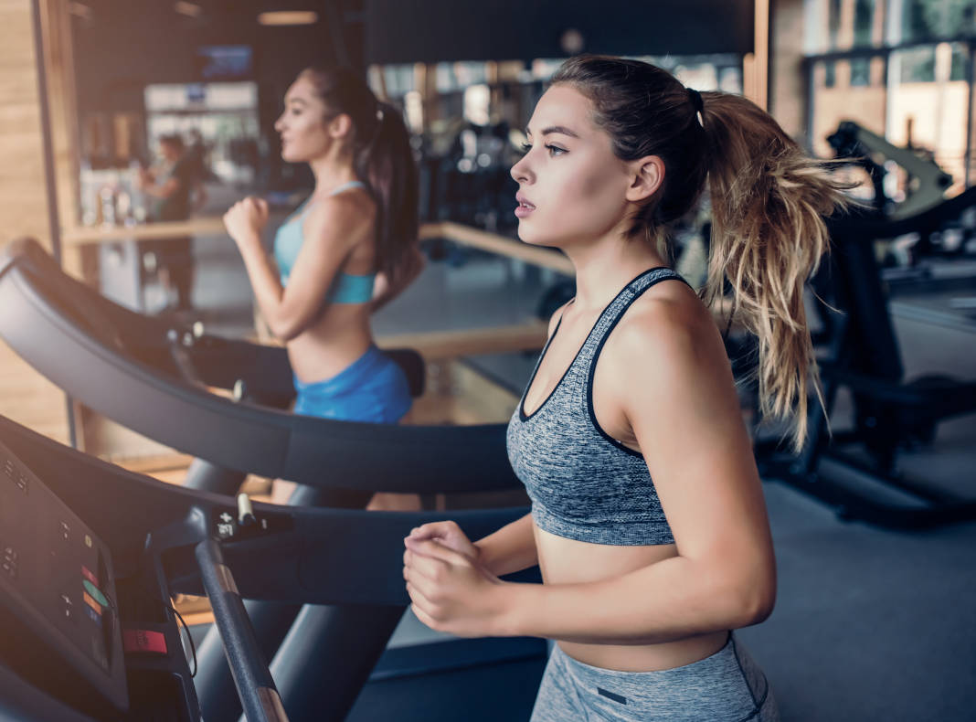 Vue de profil de 2 jeunes femmes sur un tapis de course dans une salle de sport à Marseille