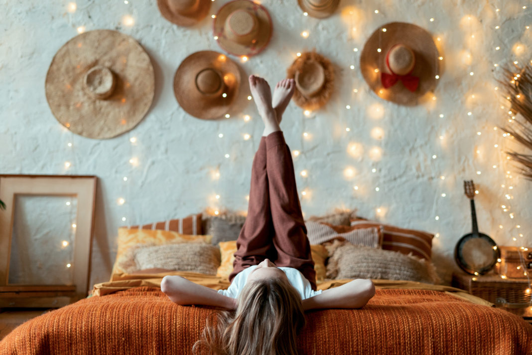 jeune femme allongée les pieds en l'air sur un lit dans une chambre cocooning à la décoration bohème