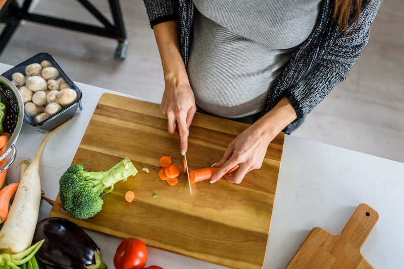 une femme enceinte en train de couper des légumes sur une planche à découper