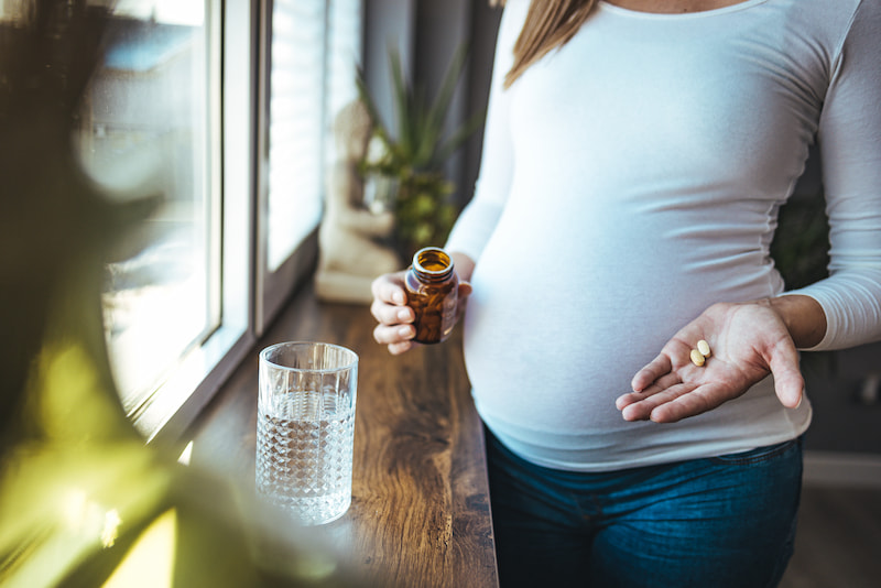 Une femme enceinte avec des compléments alimentaires dans la main et un verre d'eau posé sur une table à côté d'elle